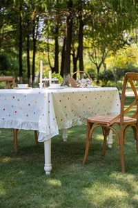 Close-up of white cotton tablecloth featuring colorful floral embroidery and ruffled edges