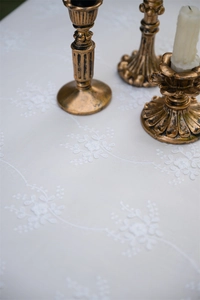 Detailed close-up of white floral embroidery on a French vintage cotton lace tablecloth
