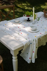 Detail of white cotton tablecloth with colorful floral embroidery and ruffled edge decor