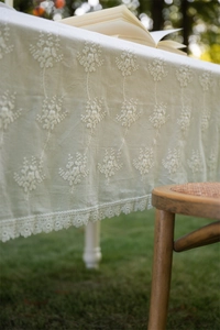 Detailed close-up of French white lace tablecloth with floral embroidery and ruffled edges