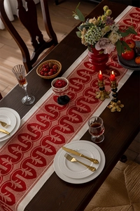 Detail of red and white jacquard table runner with leaf patterns on dark wood table