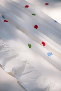 Detailed close-up of colorful floral embroidery and ruffled edge on white cotton tablecloth