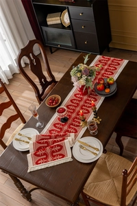 Detail of red and white jacquard table runner with decorative tassels on wooden table