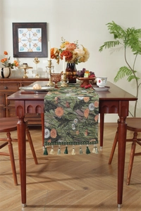 Close-up of vintage floral table runner with deep green tassels and woven texture
