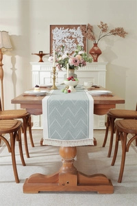 Close-up of geometric jacquard pattern on sage green table runner with white tassels
