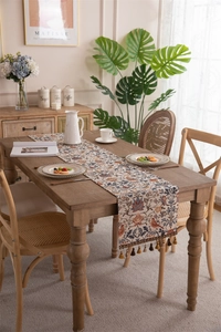 Detail of vintage floral table runner with colorful tassels on a wooden dining table