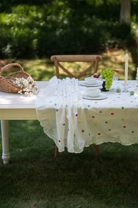 Close-up of white cotton tablecloth featuring colorful floral embroidery and ruffled edges