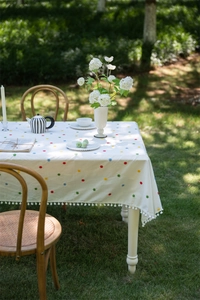 Detail of floral cotton tablecloth featuring colorful embroidery and white pom-pom trim edge