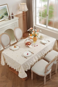 Close-up of cream cotton tablecloth featuring floral embroidery and ruffled edge design