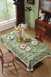 Detail of green floral jacquard tablecloth with white tassel edges on wooden table
