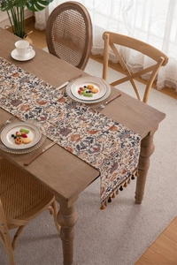 Detail of vintage floral jacquard table runner with decorative tassels on wooden table