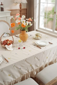 Close-up of cream cotton tablecloth with delicate floral embroidery and ruffled edge