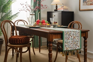 Detail of vintage floral table runner with tassels on a dark wood dining table