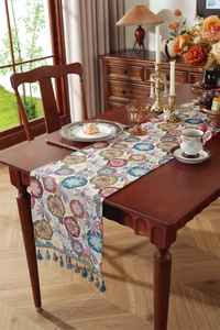 Close-up of vintage floral jacquard table runner with decorative fringe on a wooden table