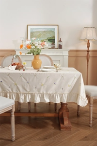 Detailed close-up of beige cotton tablecloth with floral embroidery and ruffle edge