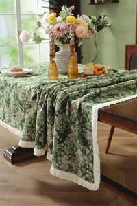 Detail of dark green floral jacquard tablecloth with creamy white fringe on a wooden table