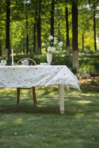 Close-up of cotton tablecloth featuring colorful floral embroidery and pom-pom fringe edge