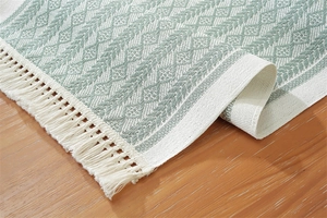 Detail of sage green geometric jacquard table runner with white fringe on wooden table