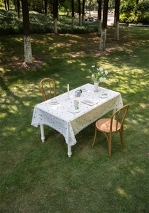 Detail of white cotton tablecloth with floral embroidery and white pom-pom trim outdoors