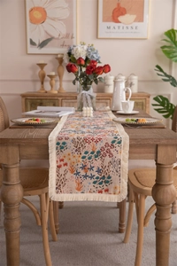 Detail of vintage floral table runner with tassel edges on a wooden dining table