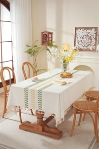 Detail of embroidered green and orange coffee leaves and fringe on beige linen tablecloth
