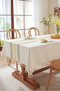 Close-up of embroidered coffee leaf pattern and tassel edge on linen tablecloth