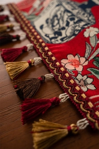 Gros plan d'un chemin de table jacquard rouge avec motifs floraux et pompons soyeux