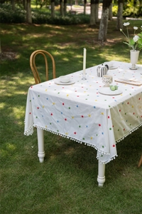 Detail of white cotton tablecloth featuring colorful floral embroidery and pom-pom fringe