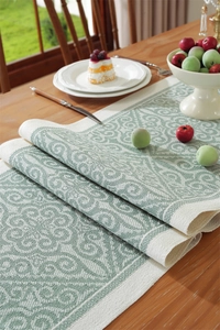 Detail of green floral jacquard table runner with baroque pattern on wooden dining table