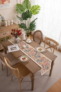 Detail of vintage floral table runner with white fringe tassels on a wooden surface