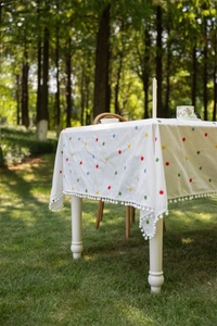 Detail of white cotton tablecloth with floral embroidery and white pom-pom fringe