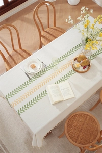 Close-up of embroidered leaf patterns and tassel fringes on beige linen tablecloth