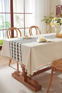 Close-up of beige linen table runner with black geometric embroidery and tassel fringe edges