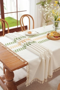 Close-up of embroidered green leaves and tassels on a beige linen tablecloth surface