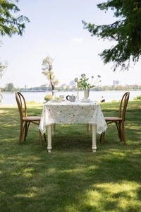 Detail of cotton tablecloth with colorful floral embroidery and white pom-pom trim edge