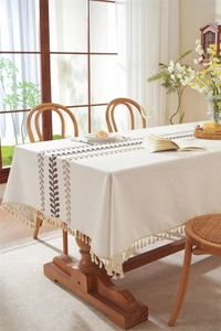 Close-up of beige linen tablecloth with brown leaf embroidery and elegant tassel fringe