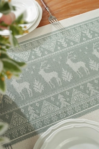Detail of jacquard table runner with deer patterns and fringe on a wooden table