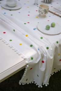 Close-up of white cotton tablecloth featuring colorful floral embroidery and pom-pom fringe