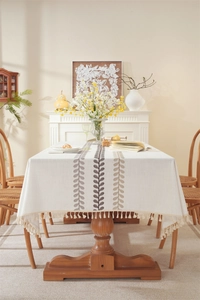Detailed close-up of embroidered coffee leaf pattern and beige tassels on cotton linen tablecloth