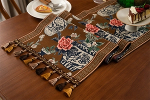 Détail du chemin de table jacquard avec motifs de pivoines et pompons sur bois sombre