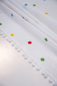 Detail of white cotton tablecloth showing colorful floral embroidery and pom-pom fringe edges