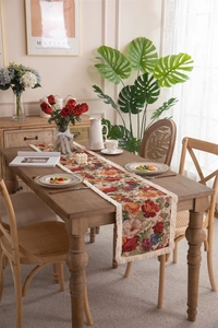 Detail of vintage floral table runner with jacquard weave and white fringe tassels on wood