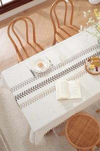Detailed embroidery of coffee leaves on a beige linen tablecloth with delicate white fringes