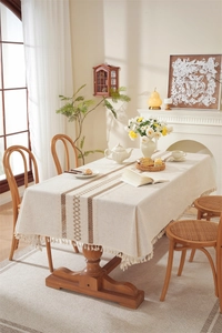 Detailed view of beige linen table runner with brown embroidery and delicate tassels