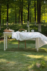 Detail of white cotton tablecloth featuring colorful floral embroidery and pom-pom trim edge