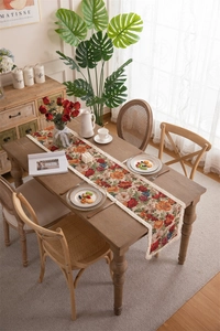 Detailed close-up of retro floral table runner with cream fringe on a wooden table