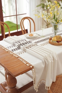 Detail of embroidered coffee leaf pattern on beige tablecloth with elegant fringe trim