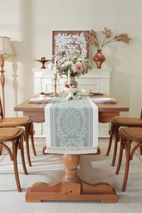 Detail of sage green jacquard table runner with intricate vine patterns and cream tassels