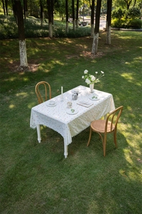 Detail of white cotton tablecloth with colorful floral embroidery and white pom-pom trim