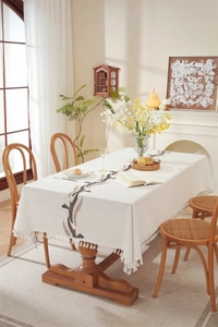 Close-up of beige linen tablecloth featuring embroidered leaves and white tassel trim